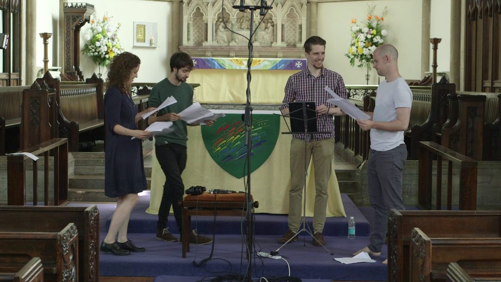 Four singers stand around a microphone in a large church.